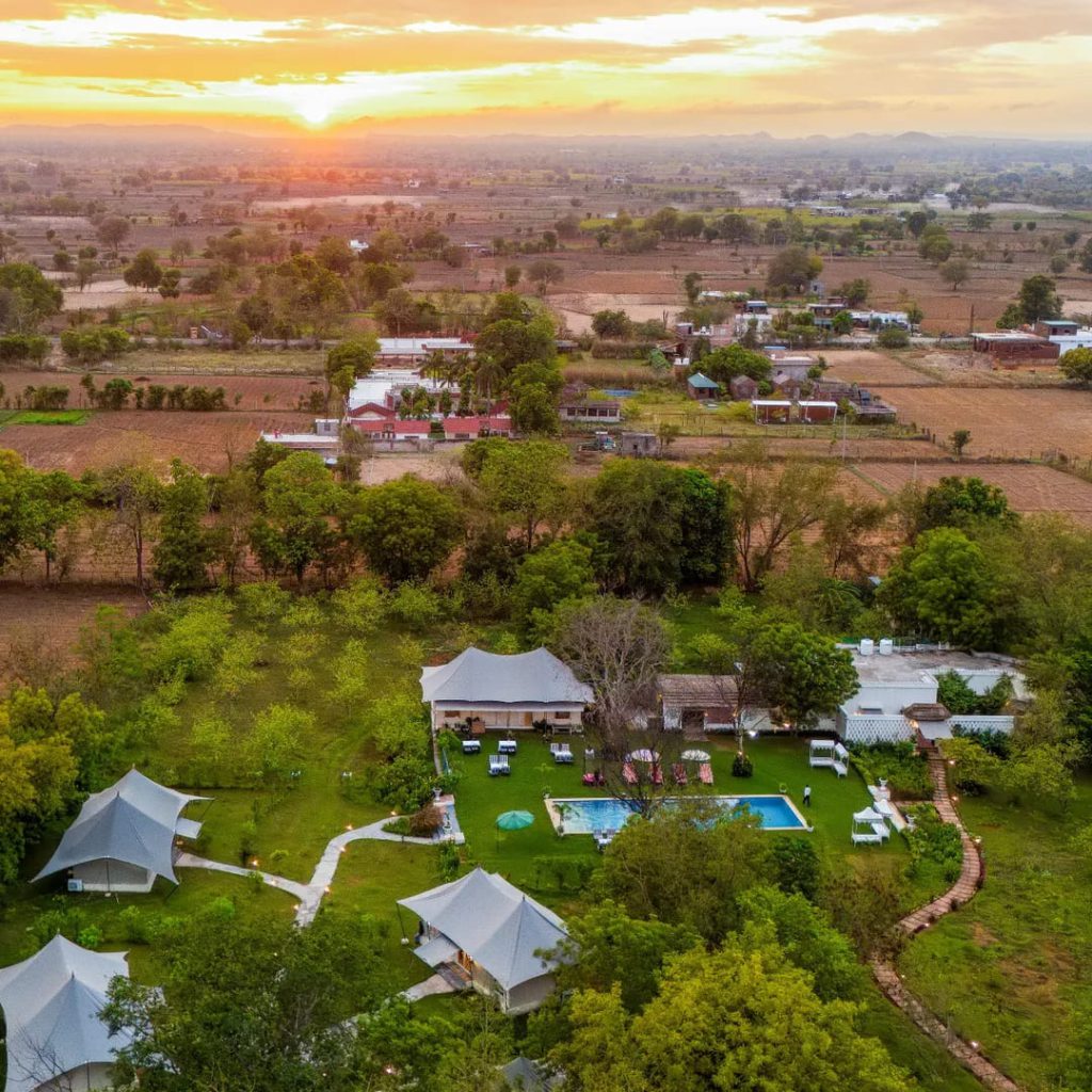 Aerial view of luxury tent resort surrounded by greenery during golden sunset
