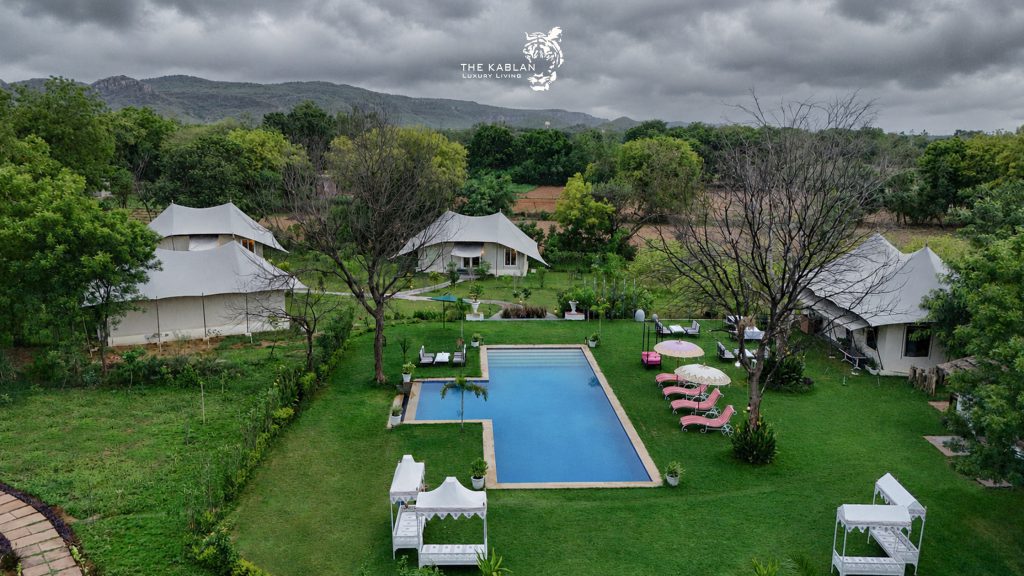 Luxury glamping resort with pool, safari tents, lush gardens, and stormy mountain backdrop.