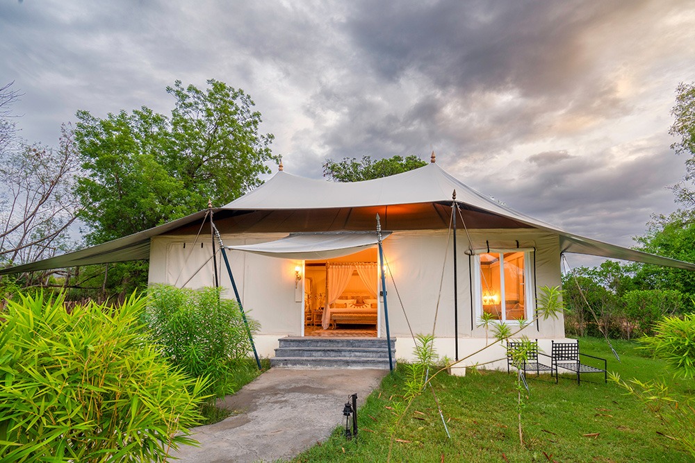 Luxury safari tent with elegant interiors, lush gardens, and dramatic cloudy evening sky.